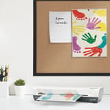 Plastifieuse à pochettes de bureau iLAM Home A3 Blanche LEITZ - La plastifieuse à pochettes Leitz iLAM Home A3 posée sur un bureau, un document engagé dans la fente